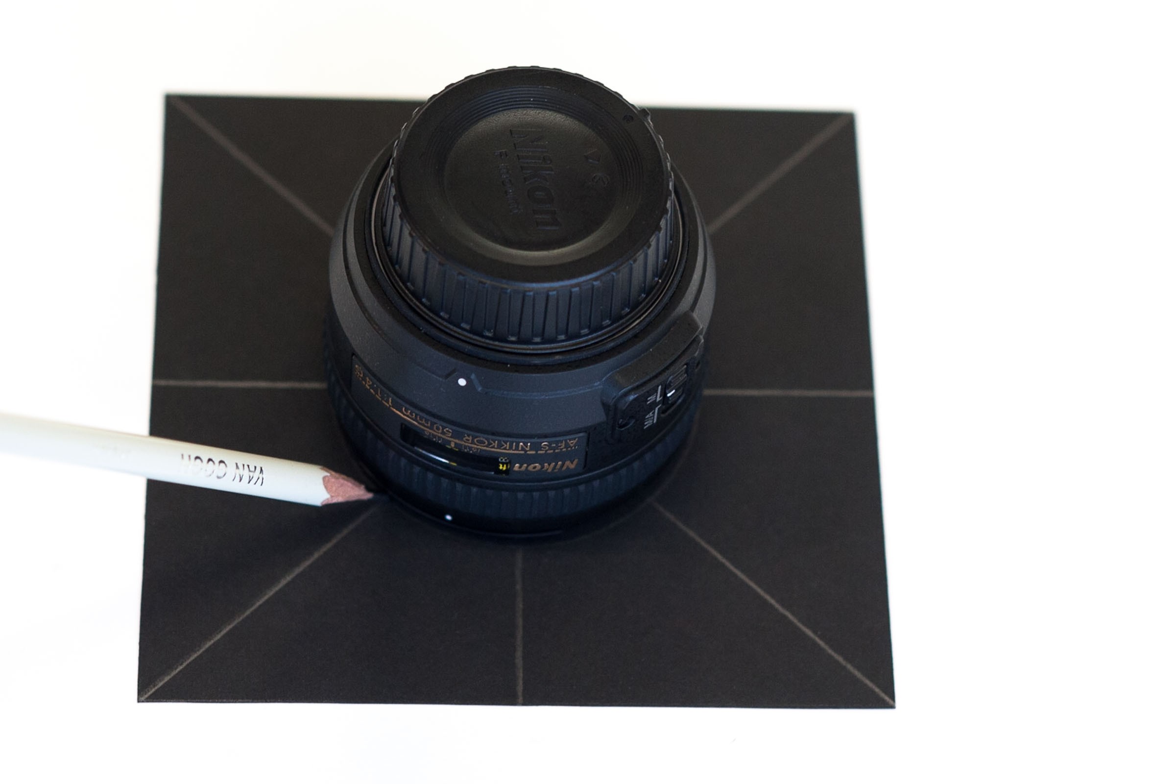 Zet het objectief met de 'glaskant' omlaag op het zwart karton. Plaats 'm precies in het midden en omcirkel het objectief hierna.