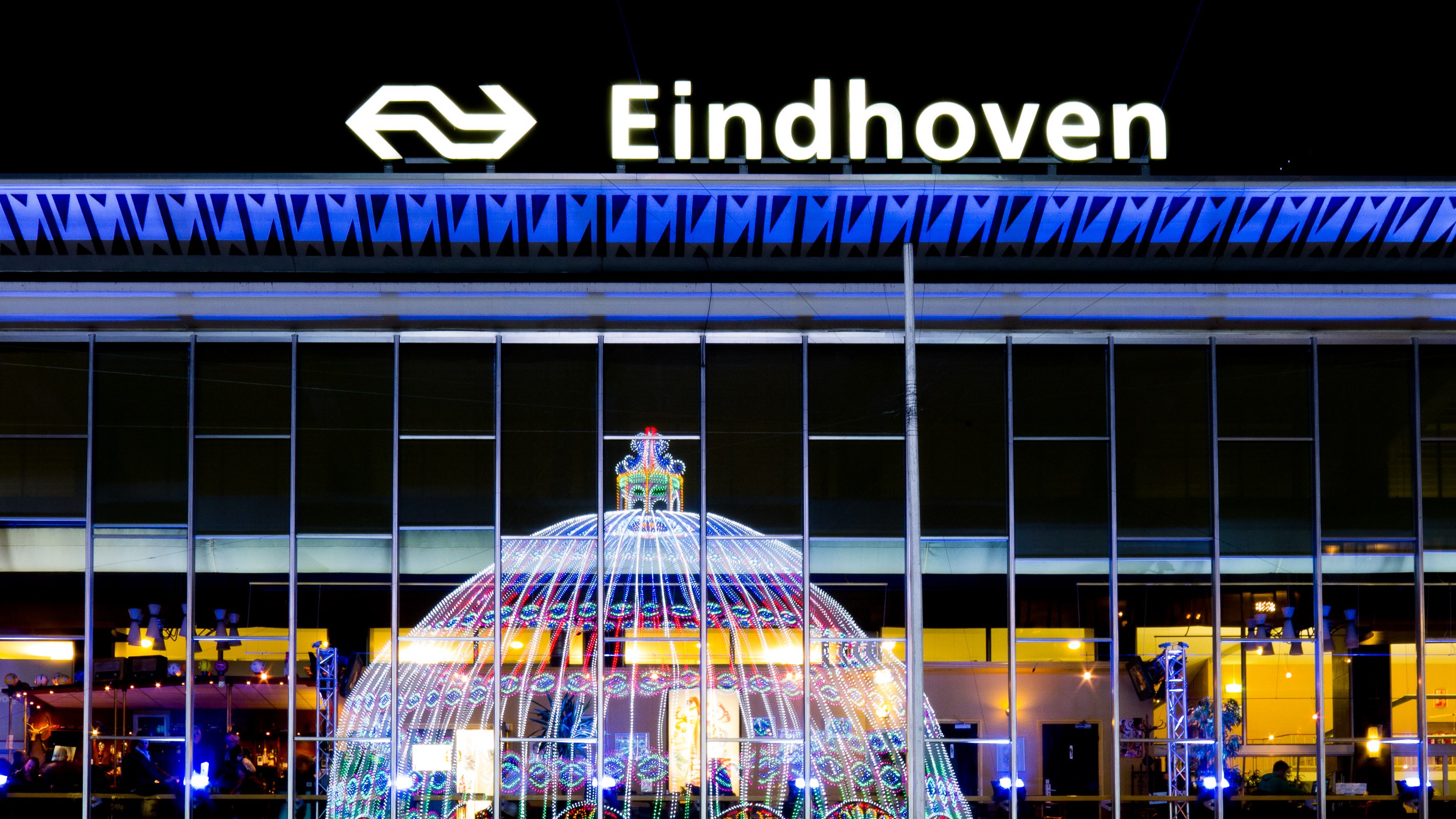 Voor het station in Eindhoven stond een enorme koepel met gekleurde LED-lampjes. In plaats van de koepel van een afstandje in beeld te brengen, fotografeerde ik de reflectie in de ramen van het station.