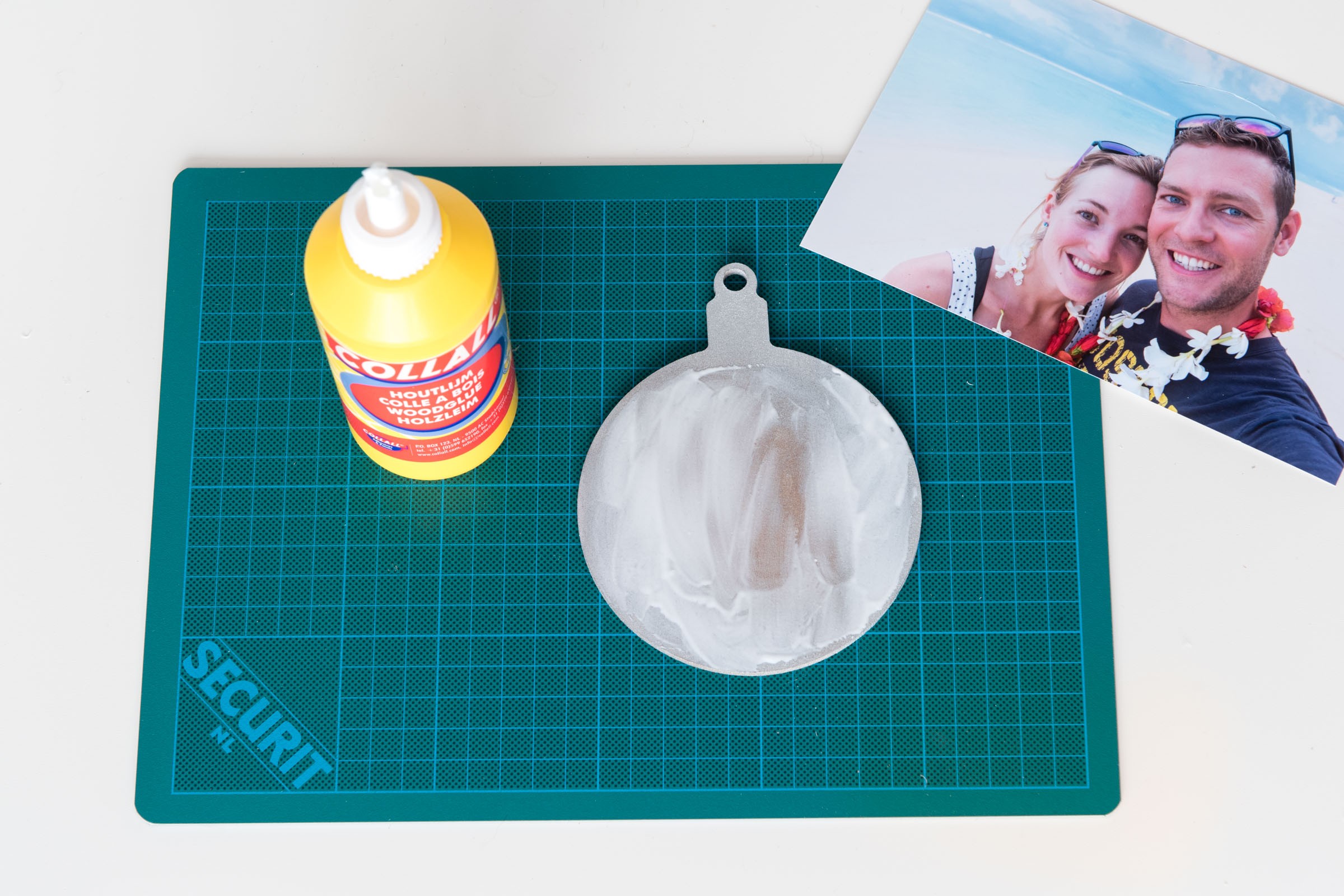 Smeer de lijm op de kerstbal. Verspreid de lijm goed tot het randje, zodat de foto goed blijft zitten.